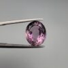 ​A 6.89-carat natural Brazilian Amethyst (Katela) gemstone with a professional oval faceted cut, displaying a deep purple hue and high transparency, held in jeweler's tweezers.