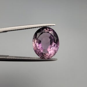 ​A 6.89-carat natural Brazilian Amethyst (Katela) gemstone with a professional oval faceted cut, displaying a deep purple hue and high transparency, held in jeweler's tweezers.