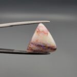 A 14.83-carat natural Australian White Opal with vibrant red, green, and yellow fire, showing unique natural dark and red surface inclusions, held in jeweler's tweezers.