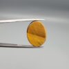 ​A 16.36-carat natural Golden Tiger's Eye oval cabochon with brilliant chatoyant bands and rich earthy tones, held in jeweler's tweezers.