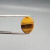 A premium 17.17-carat natural Golden Tiger's Eye oval cabochon with brilliant high-luster chatoyancy and deep chocolate-amber banding, held in jeweler's tweezers.