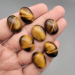 A set of seven natural Golden Tiger's Eye oval cabochons, showing high-luster golden chatoyancy and rich brown banding, arranged together.