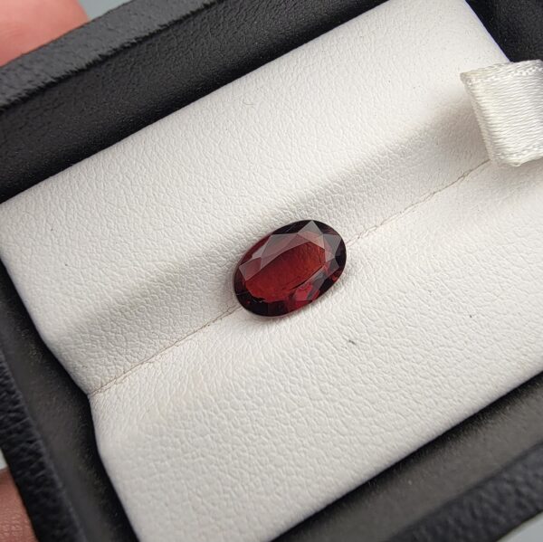 A 2.35-carat natural oval-cut Madagascar Garnet with a deep crimson red hue and high-luster facets, presented in a black jewelry box.