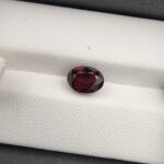 A 2.69-carat natural oval-cut Madagascar Garnet with a deep red color and high-clarity facets, presented in a clear jeweler's display case.