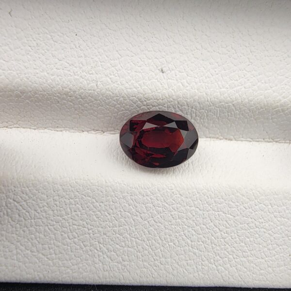 A 2.69-carat natural oval-cut Madagascar Garnet with a deep red color and high-clarity facets, presented in a clear jeweler's display case.