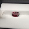 A 2.50-carat natural oval-cut Madagascar Garnet featuring a rich crimson red color and high-clarity facets, presented in a jeweler's display case.