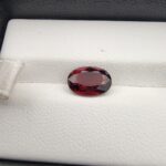 A 2.50-carat natural oval-cut Madagascar Garnet featuring a rich crimson red color and high-clarity facets, presented in a jeweler's display case.