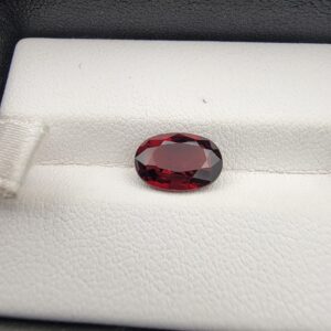 A 2.50-carat natural oval-cut Madagascar Garnet featuring a rich crimson red color and high-clarity facets, presented in a jeweler's display case.