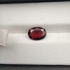 A 2.50-carat natural oval-cut Madagascar Garnet featuring a rich crimson red color and high-clarity facets, presented in a jeweler's display case.