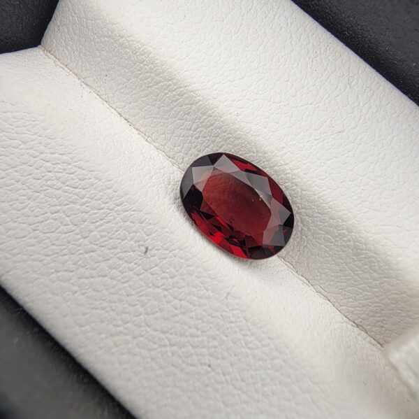 A 2.50-carat natural oval-cut Madagascar Garnet featuring a rich crimson red color and high-clarity facets, presented in a jeweler's display case.