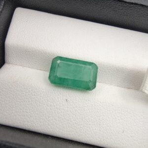 ​A 5-carat natural Zambian Emerald featuring a deep green color and a classic step-cut emerald shape, displayed in a clear gemstone case.