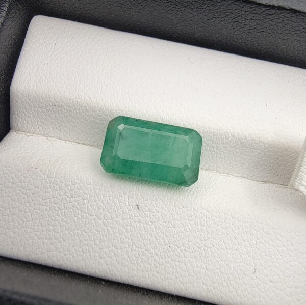 ​A 5-carat natural Zambian Emerald featuring a deep green color and a classic step-cut emerald shape, displayed in a clear gemstone case.