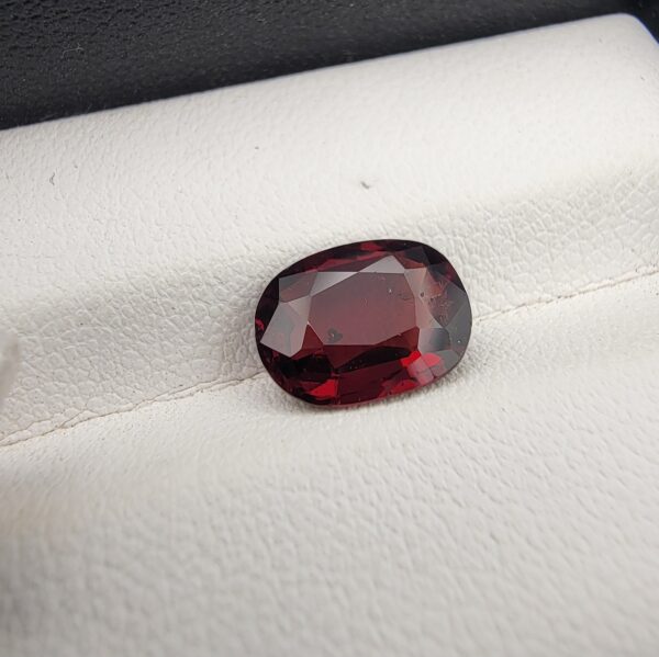 A 3.26-carat natural oval-cut Madagascar Garnet featuring a rich deep red color and high-clarity facets, displayed in a gemstone case.