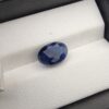 ​A 4.87-carat natural Ceylon blue sapphire with a deep blue color and oval faceted cut, presented in a white jeweler's box.