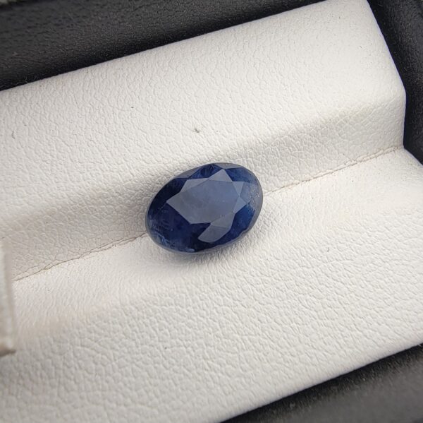 ​A 4.87-carat natural Ceylon blue sapphire with a deep blue color and oval faceted cut, presented in a white jeweler's box.