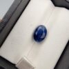 ​A 4.87-carat natural Ceylon blue sapphire with a deep blue color and oval faceted cut, presented in a white jeweler's box.