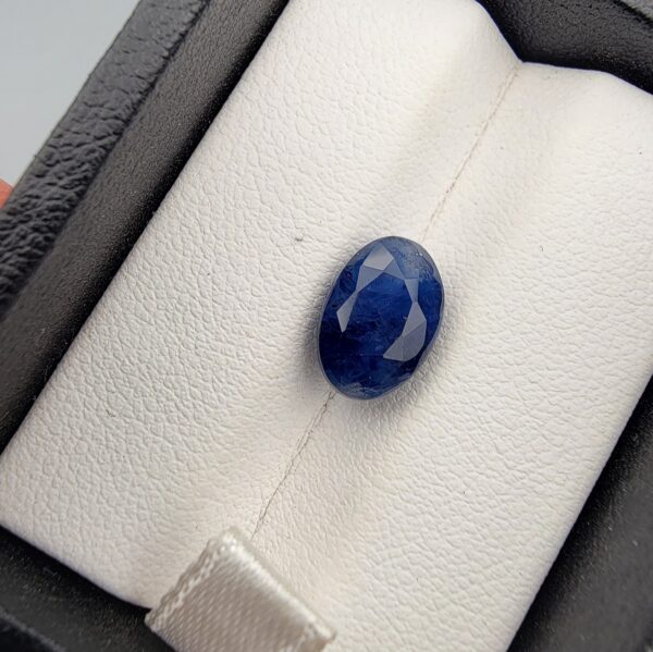 ​A 4.87-carat natural Ceylon blue sapphire with a deep blue color and oval faceted cut, presented in a white jeweler's box.