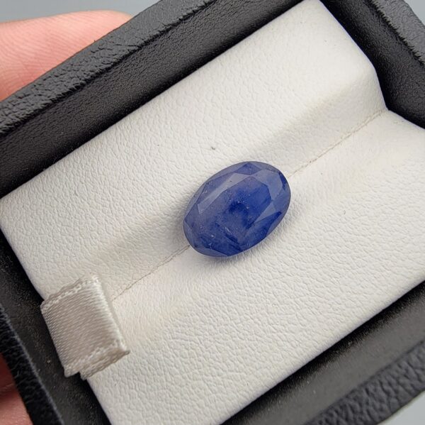 ​A large 6.30-carat natural Ceylon blue sapphire with a rich blue color and oval faceted cut, presented in a white jeweler's box.