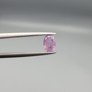 A 0.65-carat natural Ceylon purple sapphire featuring unique black mountain-desert inclusions and an oval faceted cut, displayed in a white jeweler's box.
