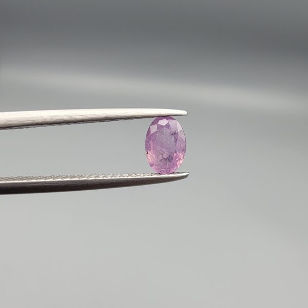 A 0.65-carat natural Ceylon purple sapphire featuring unique black mountain-desert inclusions and an oval faceted cut, displayed in a white jeweler's box.