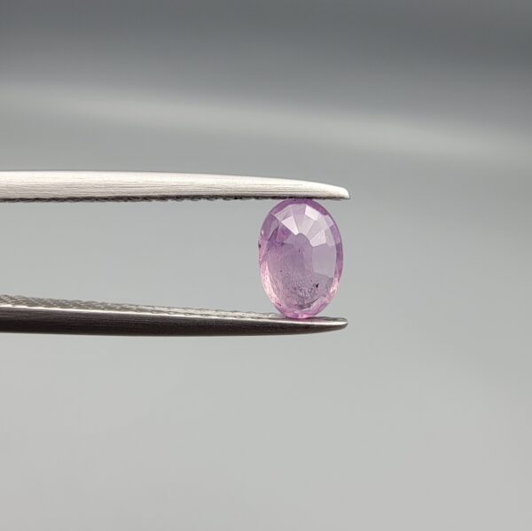 A 0.65-carat natural Ceylon purple sapphire featuring unique black mountain-desert inclusions and an oval faceted cut, displayed in a white jeweler's box.