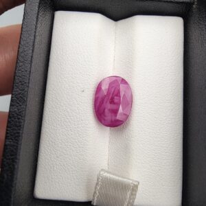 ​A 4.67-carat natural Mozambique Ruby with a pinkish-red color and oval faceted cut, displayed in a white jeweler's box.