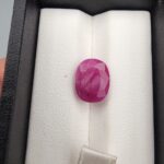 ​A 6.74-carat natural Mozambique Ruby with a pinkish-red color and oval faceted cut, displayed in a white jeweler's box.