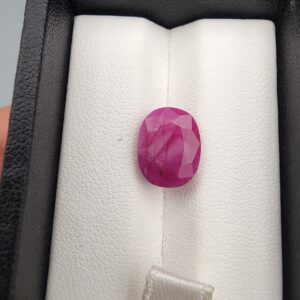 ​A 6.74-carat natural Mozambique Ruby with a pinkish-red color and oval faceted cut, displayed in a white jeweler's box.