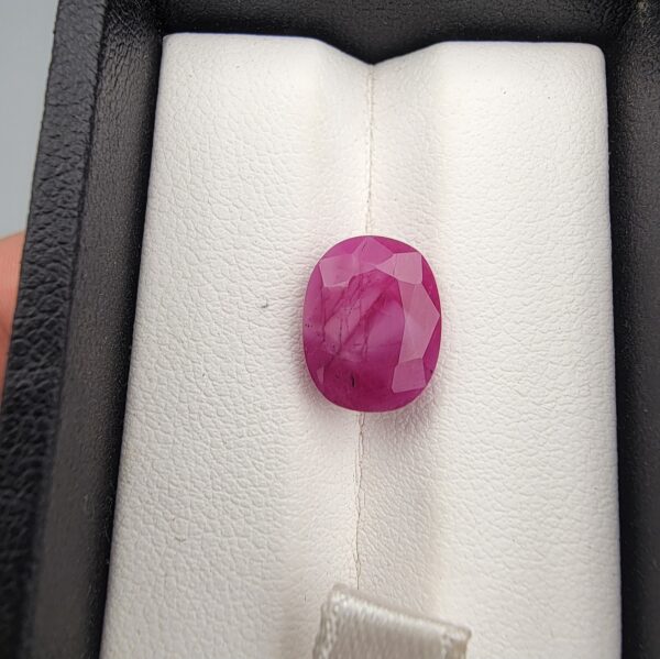 ​A 6.74-carat natural Mozambique Ruby with a pinkish-red color and oval faceted cut, displayed in a white jeweler's box.