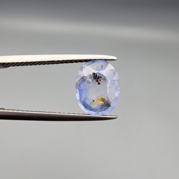A 2.17-carat natural Ceylon blue sapphire with unique internal black and yellow inclusions, featuring an oval faceted cut and transparent blue body.