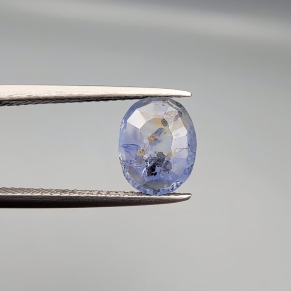 A 2.17-carat natural Ceylon blue sapphire with unique internal black and yellow inclusions, featuring an oval faceted cut and transparent blue body.