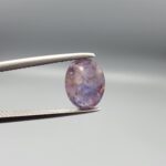 ​A 2.96-carat natural Ceylon purple sapphire with a transparent violet-purple color and oval faceted cut, shown in a white jeweler's box under professional lighting.