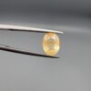 ​A 2-carat natural Ceylon yellow sapphire with an oval faceted cut and visible golden internal inclusions, shown in a white jeweler's box.