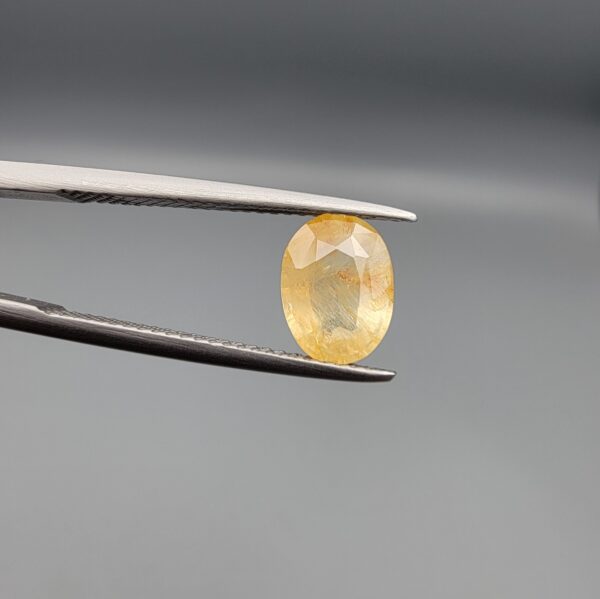 ​A 2-carat natural Ceylon yellow sapphire with an oval faceted cut and visible golden internal inclusions, shown in a white jeweler's box.