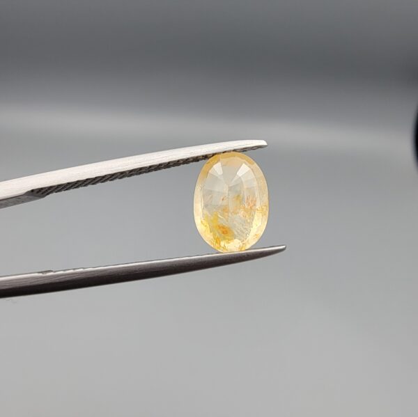 ​A 2-carat natural Ceylon yellow sapphire with an oval faceted cut and visible golden internal inclusions, shown in a white jeweler's box.
