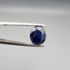 A 3.95-carat natural Ceylon blue sapphire with a deep blue hue and oval faceted cut, shown resting on a black and white textured jewelry display.