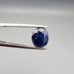 A 3.95-carat natural Ceylon blue sapphire with a deep blue hue and oval faceted cut, shown resting on a black and white textured jewelry display.
