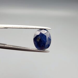 A 3.95-carat natural Ceylon blue sapphire with a deep blue hue and oval faceted cut, shown resting on a black and white textured jewelry display.