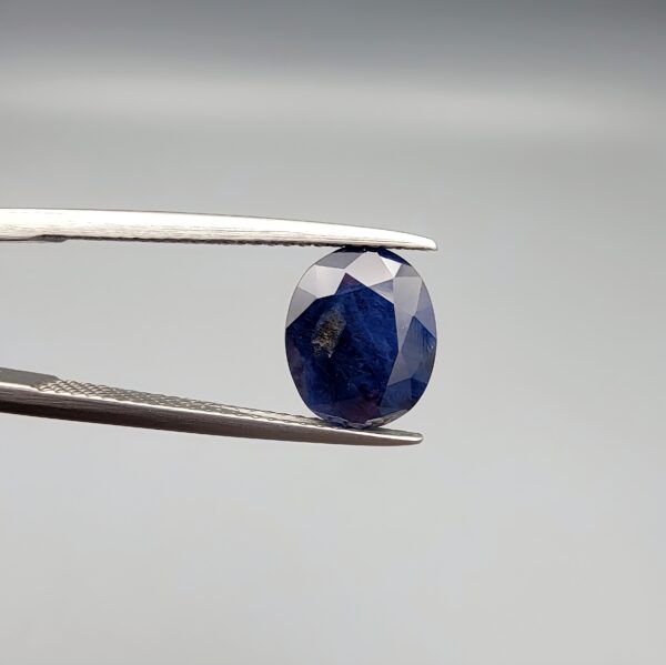 A 3.95-carat natural Ceylon blue sapphire with a deep blue hue and oval faceted cut, shown resting on a black and white textured jewelry display.