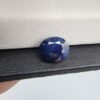 A 3.95-carat natural Ceylon blue sapphire with a deep blue hue and oval faceted cut, shown resting on a black and white textured jewelry display.