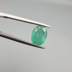 ​A 1.50-carat natural Zambian emerald with a vivid green color and oval faceted cut, displayed in a white jeweler's box.