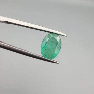 ​A 1.50-carat natural Zambian emerald with a vivid green color and oval faceted cut, displayed in a white jeweler's box.