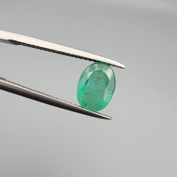​A 1.50-carat natural Zambian emerald with a vivid green color and oval faceted cut, displayed in a white jeweler's box.