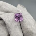 An 11.48-carat natural Brazilian amethyst with a deep purple color and professional faceted cut, displayed in a white jeweler's box under natural light.