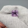 An 11.48-carat natural Brazilian amethyst with a deep purple color and professional faceted cut, displayed in a white jeweler's box under natural light.