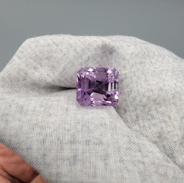 An 11.48-carat natural Brazilian amethyst with a deep purple color and professional faceted cut, displayed in a white jeweler's box under natural light.