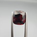 ​A 6.08-carat natural red garnet from Madagascar, featuring a deep reddish color and sparkling faceted cut, professionally displayed in a white jeweler's box.