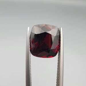 ​A 6.08-carat natural red garnet from Madagascar, featuring a deep reddish color and sparkling faceted cut, professionally displayed in a white jeweler's box.