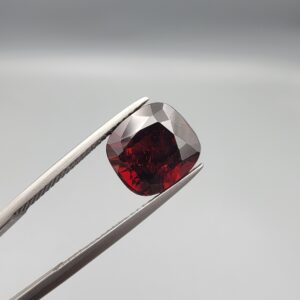 ​A 6.81-carat natural red garnet from Madagascar, featuring a deep reddish color and sparkling faceted cut, professionally displayed in a white jeweler's box.