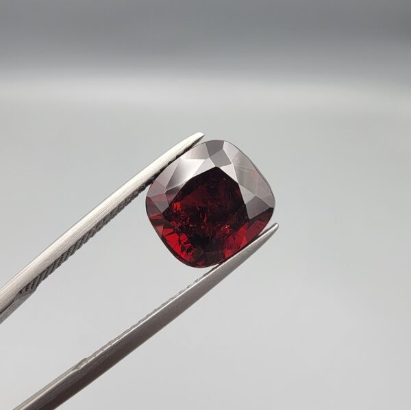 ​A 6.81-carat natural red garnet from Madagascar, featuring a deep reddish color and sparkling faceted cut, professionally displayed in a white jeweler's box.